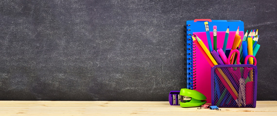 School supplies on a wood desk with chalkboard background. Side view. Back to school concept. Copy...