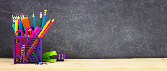 School supplies on a wood desk with chalkboard background. Side view. Back to school concept. Copy...