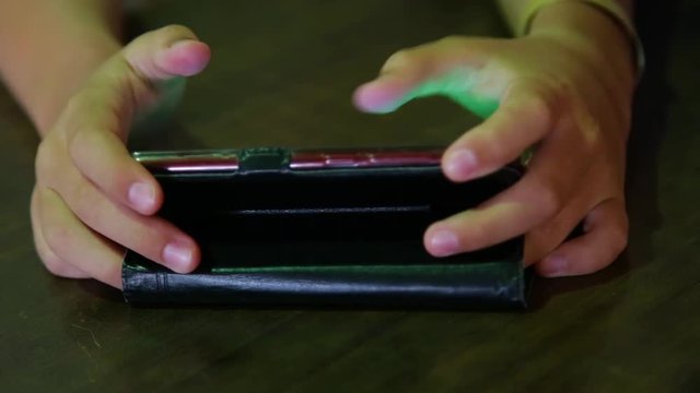 Closeup view of hands of young child sitting at table in darkness and playing computer video games using touchscreen of smartphone. Real time full hd footage.