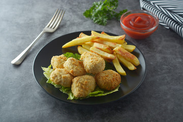 Chicken nuggets with french fries on dark background, top view.