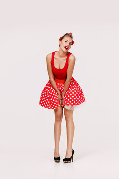 smiling pin up woman in polka dot red dress isolated on gray background. cute girl posing in retro style