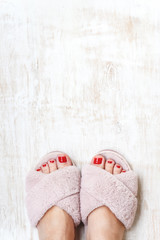 female legs with red nails in home fur fluffy pink slippers on a light wooden background. flat lay....