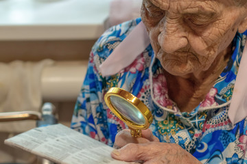 Very Old Woman with magnifier trying to Read from a newspaper. grandmother 90 years old reads at...