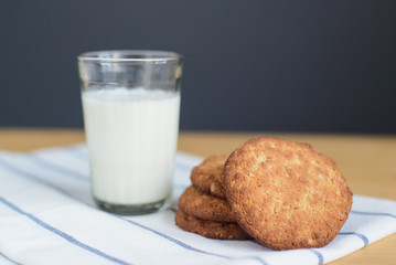 still life of round brown wholegrain flour cookies and milk glass on striped white napkin on wooden table, side view of horizontal stock photo image