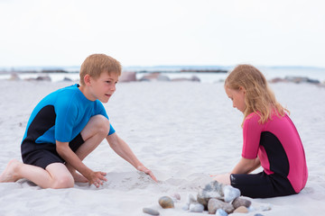 Two children in neoprene swimsuits playing on the beach with sand