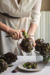 Woman wearing in white clean and cut fresh artichoke. Close up.