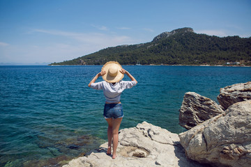 woman in a hat and shirt standing on a stone by the sea