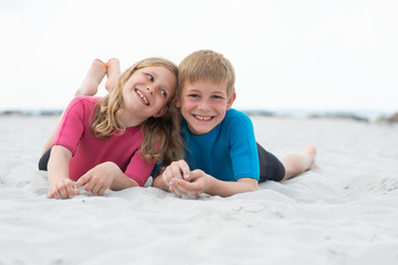 Fototapeta na wymiar Portrait of two happy children in neoprene swimsuits playing on the beach with sand