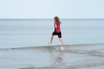 Happy little girl running in sea and playing with waves