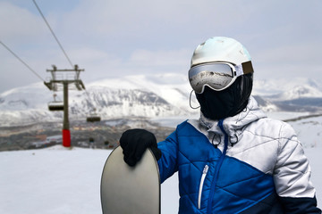 Fototapeta na wymiar snowboarder with a board in his hand stands on the top of the mountain of a ski resort amid the ski lift