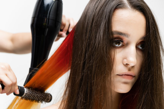 Photo portrait of the work of the master hairdresser makes a fashionable hairstyle with a hair dryer and a hairbrush in the studio on a white background. The brunette model has colored hair.