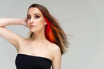Fototapeta premium A close-up portrait photo of a fashionable hairstyle red-yellow in studio on a white background. The pretty brunette model with beautiful make-up has beautiful flowing colorful hair.