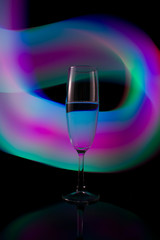 A single wine glass isolated on a black background with red white pink and orange neon light painting streaks of light behind them. Light wave, game of colors, drawing light