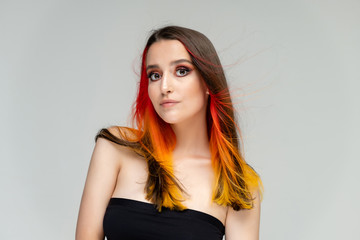 A close-up portrait photo of a fashionable hairstyle red-yellow in studio on a white background. The pretty brunette model with beautiful make-up has beautiful flowing colorful hair.