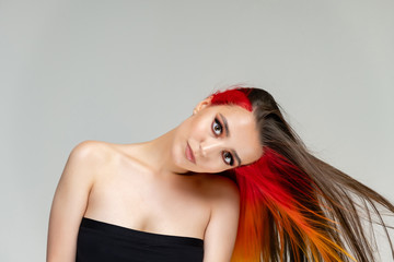 A close-up portrait photo of a fashionable hairstyle red-yellow in studio on a white background. The pretty brunette model with beautiful make-up has beautiful flowing colorful hair.