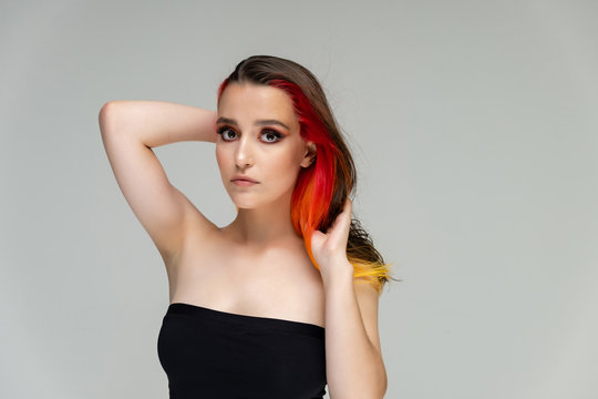 A close-up portrait photo of a fashionable hairstyle red-yellow in studio on a white background. The pretty brunette model with beautiful make-up has beautiful flowing colorful hair.