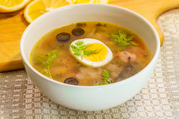 home-made salmon soup seasoned with hard-boiled egg, olives, lemon slices and dill in a white porcelain bowl