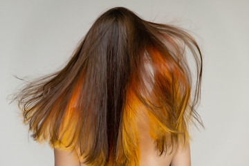 A close-up portrait photo of a fashionable hairstyle red-yellow in studio on a white background. The pretty brunette model with beautiful make-up has beautiful flowing colorful hair.