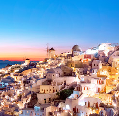 Fototapeta premium Oia at sunset. Beautiful view of the village of Oia, Santorini, Greece, Aegean sea, Europe. Classic white Greek architecture, houses, churches, windmills. Travel concept, popular place
