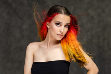 Fototapeta premium A close-up portrait photo of a fashionable hairstyle red-yellow in studio on a gray background. The pretty brunette model with beautiful make-up has beautiful flowing colorful hair.