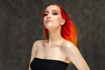 A close-up portrait photo of a fashionable hairstyle red-yellow in studio on a gray background. The pretty brunette model with beautiful make-up has beautiful flowing colorful hair.