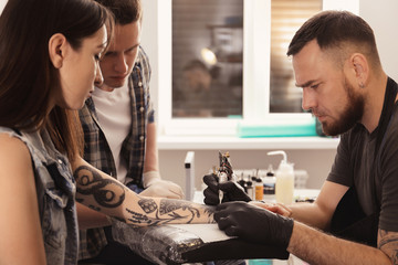 Professional tattoo master teaching young specialist in salon. Internship concept