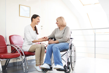 Fototapeta premium Young female doctor taking care of mature woman in wheelchair indoors