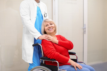 Male doctor taking care of mature woman in wheelchair indoors