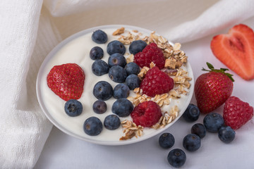 White yogurt in bowl with oatmeal and strawberries, blueberries and raspberries on the top on white background.