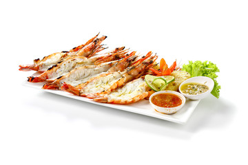 Grilled 5 black tiger shrimps with boiled potatoes, slice of lime, tomato fresh vegetables and 2 chili seafood sauce on white square plate isolated on white background with shadow low angle side view