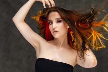 A close-up portrait photo of a fashionable hairstyle red-yellow in studio on a gray background. The pretty brunette model with beautiful make-up has beautiful flowing colorful hair.