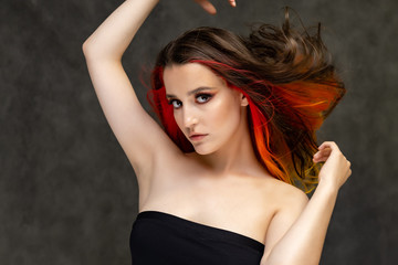 Naklejka premium A close-up portrait photo of a fashionable hairstyle red-yellow in studio on a gray background. The pretty brunette model with beautiful make-up has beautiful flowing colorful hair.