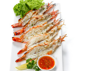 Grilled 5 black tiger shrimps with boiled potatoes, slice of lime, tomato fresh vegetables and chili seafood sauce on white square plate isolated on white background with shadow high angle top view