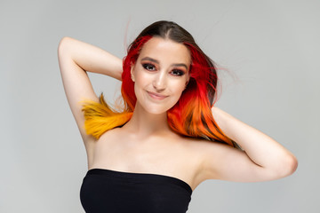 Fototapeta premium A close-up portrait photo of a fashionable hairstyle red-yellow in studio on a blue background. The pretty brunette model with beautiful make-up has beautiful flowing colorful hair.