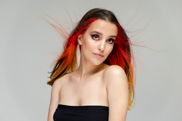 Naklejka premium A close-up portrait photo of a fashionable hairstyle red-yellow in studio on a blue background. The pretty brunette model with beautiful make-up has beautiful flowing colorful hair.