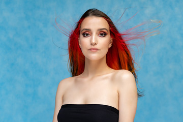 A close-up portrait photo of a fashionable hairstyle red-yellow in studio on a blue background. The...