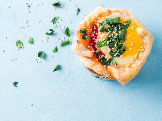 Ideas and recipes for healthy Vegan Shakshouka cups with vegan tofu eggs and turmeric yolk on blue table. Puff filo pastry, tomato and vegetable sauce, green parsley. Top view or flat lay. Copy space