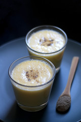 Two glasses of refreshing mango lassi drink, decorated with cardamom. Dark background, selective focus.