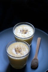 Two glasses of refreshing mango lassi drink, decorated with cardamom. Dark background, selective focus.