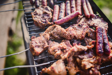 Grilling sausages on barbecue grill. Pork sausage and steak in smoke. Close-up view & Selective focus. 