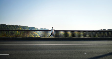 woman with quick walk crosses bridge across river along railing on city street, returns home from...