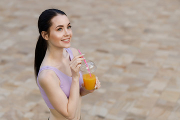 Young beautiful girl drinking fresh juice from plastic cup take-out food after fitness running workout outdoor. Healthy lifestyle. Smiling slim brunette woman with lemonade.