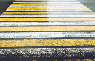 Slippery road with a pedestrian crossing painted in yellow and white Zebra with glare after rain.