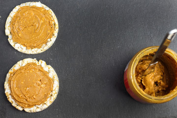 crunchy natural peanut butter sandwich  on rice cake bread on black slate background with jar peanut butter with knife with free copy space. Proper nutrition diet vegetarian breakfast