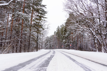Patterns on the winter highway in the form of four straight lines. Snowy road on the background of snow-covered forest. Winter landscape.