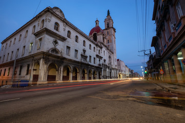Street view of the busy road with traffic  with Catholic Church building in the background in the Old Havana City, Capital of Cuba, during night time after sunset.