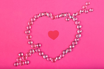Heart lined with beads with an arrow on a pink background with a heart in the middle.