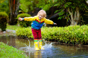 Child playing in puddle. Kids jump in autumn rain