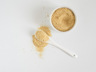 Nutritional yeast. Nutritional inactive yeast in small white ctramic bowl and white ceramic spoon....