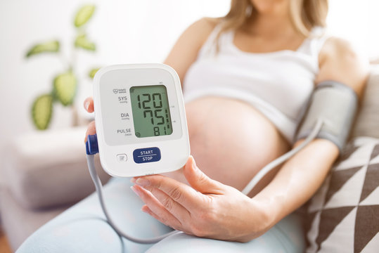 Pregnant woman in bed measures blood pressure, self-diagnosis, health care.